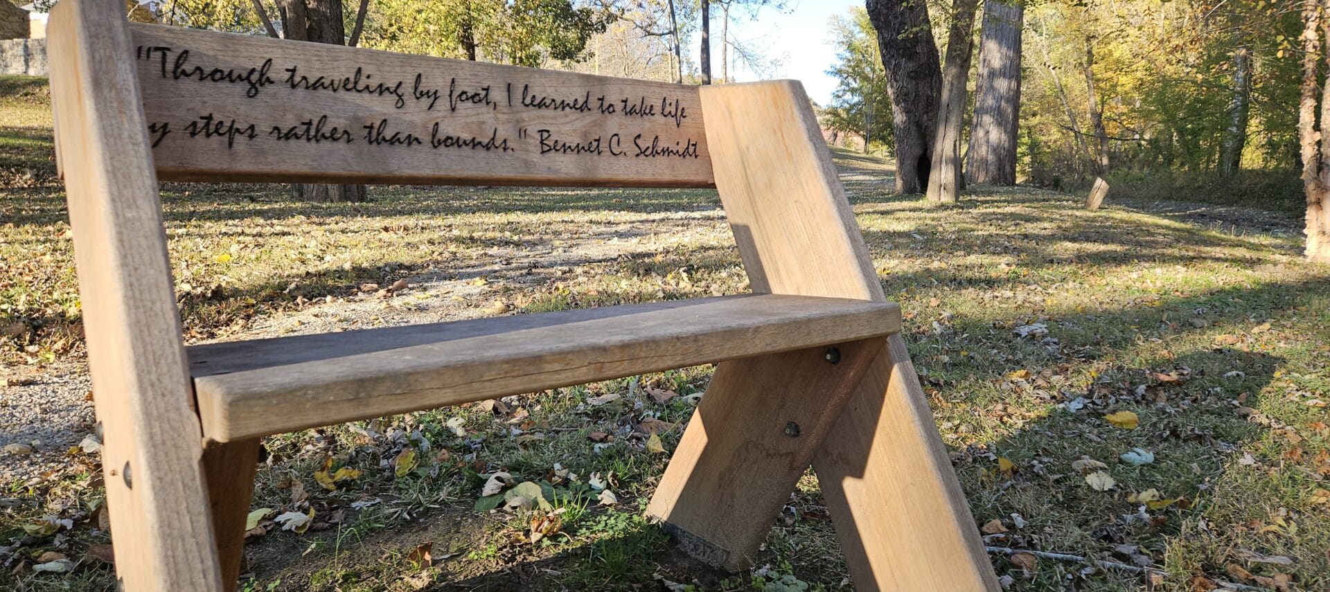 wooden bench with quote inscribed on back panel, in a scenic nature area