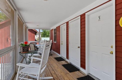White rocking chairs on long wooden porch in front of rooms