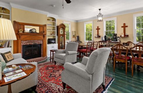 Great room with cream walls, white trim, teal hardwood flooring, multiple dining tables, sitting area, and fireplace