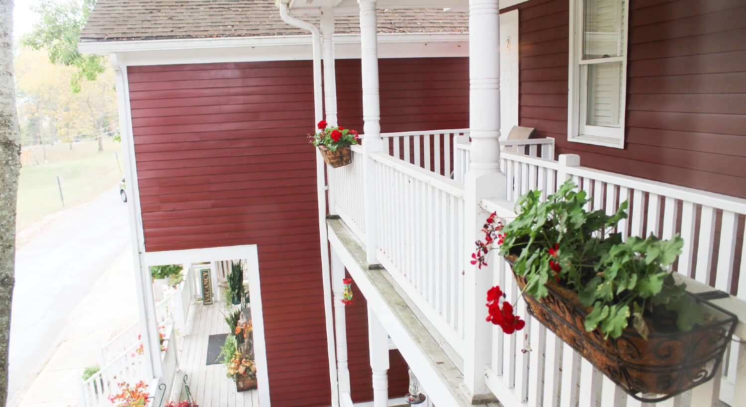 side-view of red house with white trimmed windows with white pillared balcony with flower box looking down to front porch