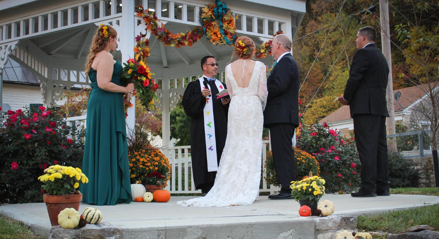bride and groom standing in front of minister by white gazebo, best man and maid of honor standing next to couple