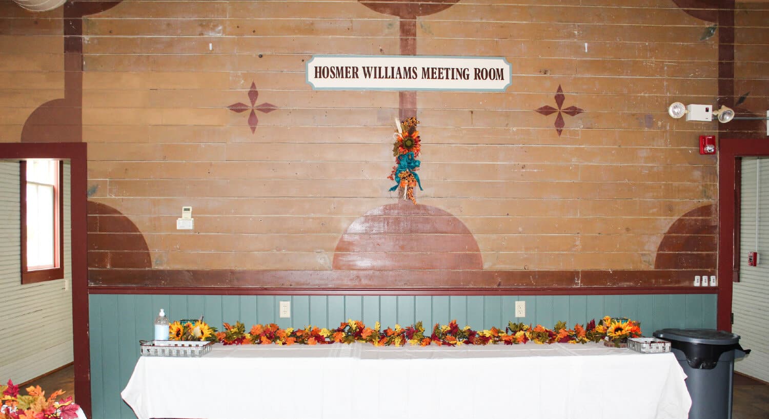 hosmer williams meeting room on brown wood with buffet table with white table close decorated with fall flowers and flower arrangement hanging on wall