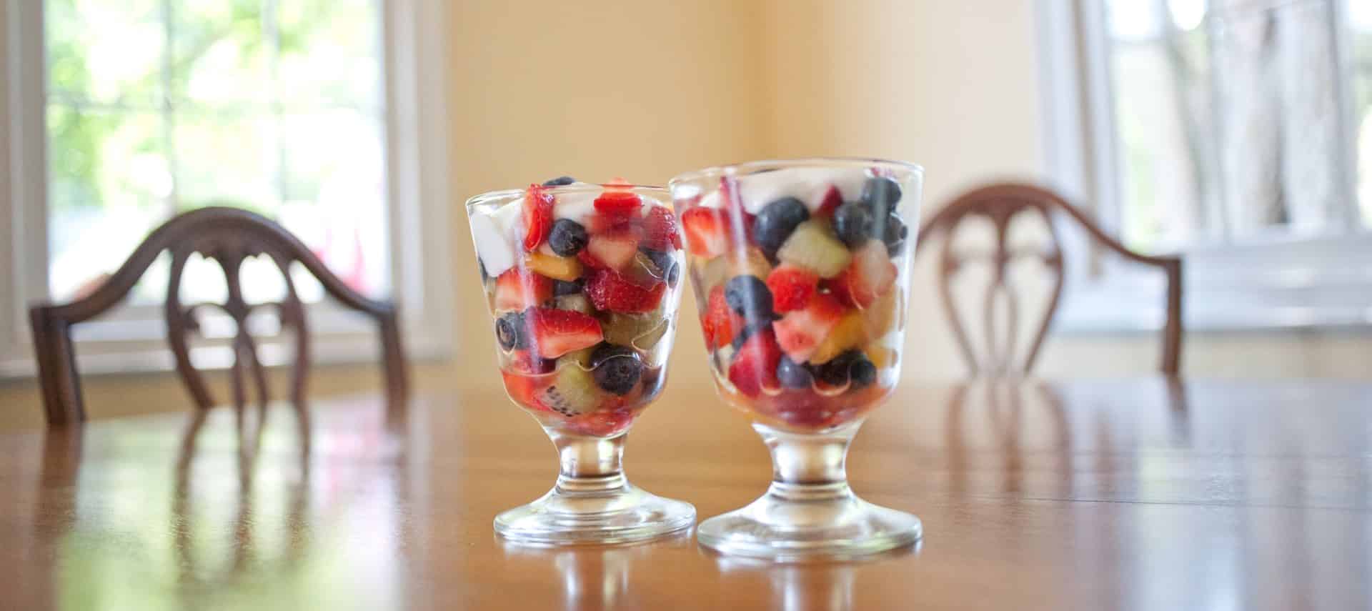 Two fruit parfaits in glass cups on top of wooden table