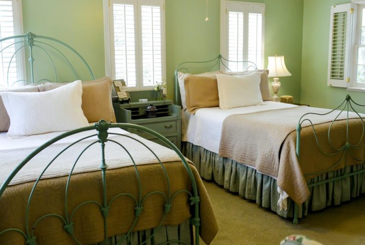 Two full size beds with neutral colored bedding in light green room