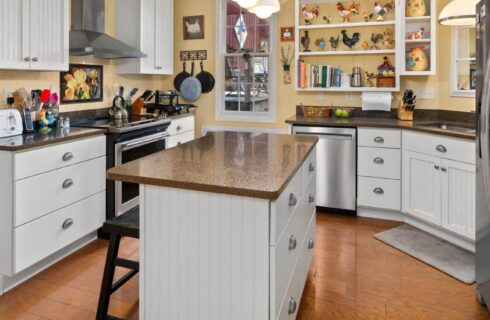 Kitchen with yellow walls, white trim, hardwood flooring, stainless steel appliances, white cabinets, and quartz countertops