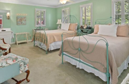 Bedroom with light green walls, white trim, carpeting, two beds, and sitting area