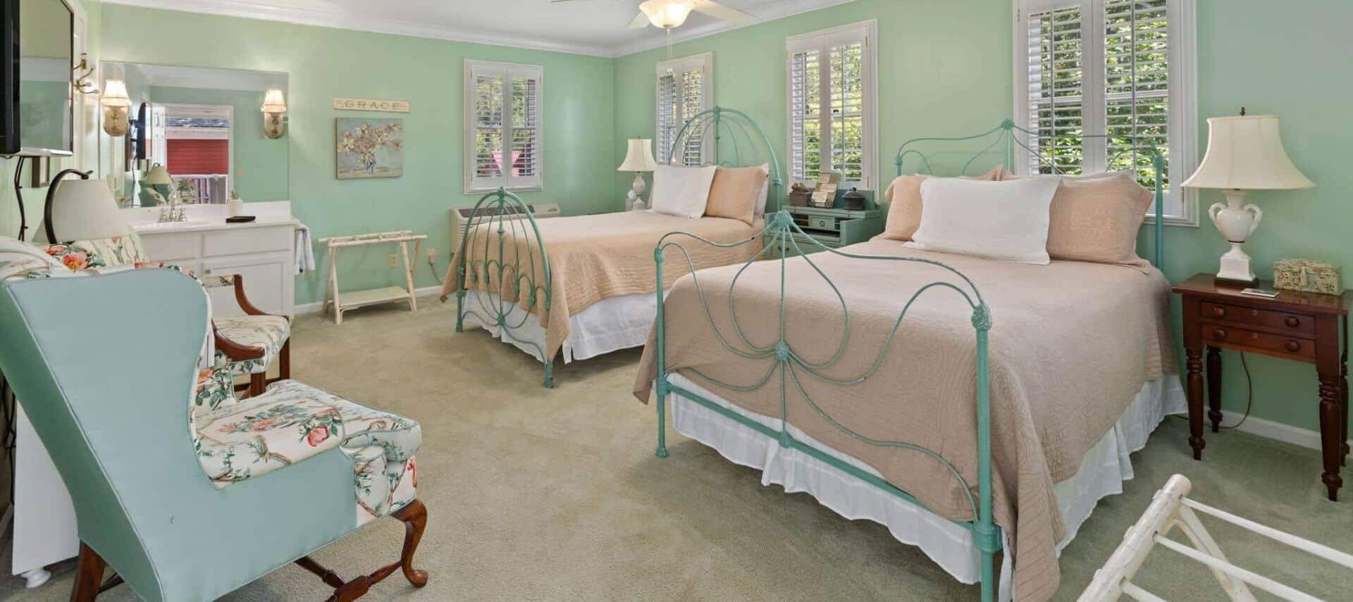 Bedroom with light green walls, white trim, carpeting, two beds, and sitting area