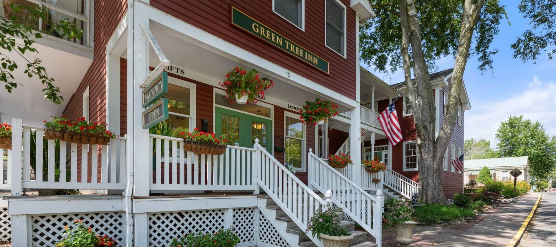 Large home painted dark red with white trim and green door, hanging plants and american flag