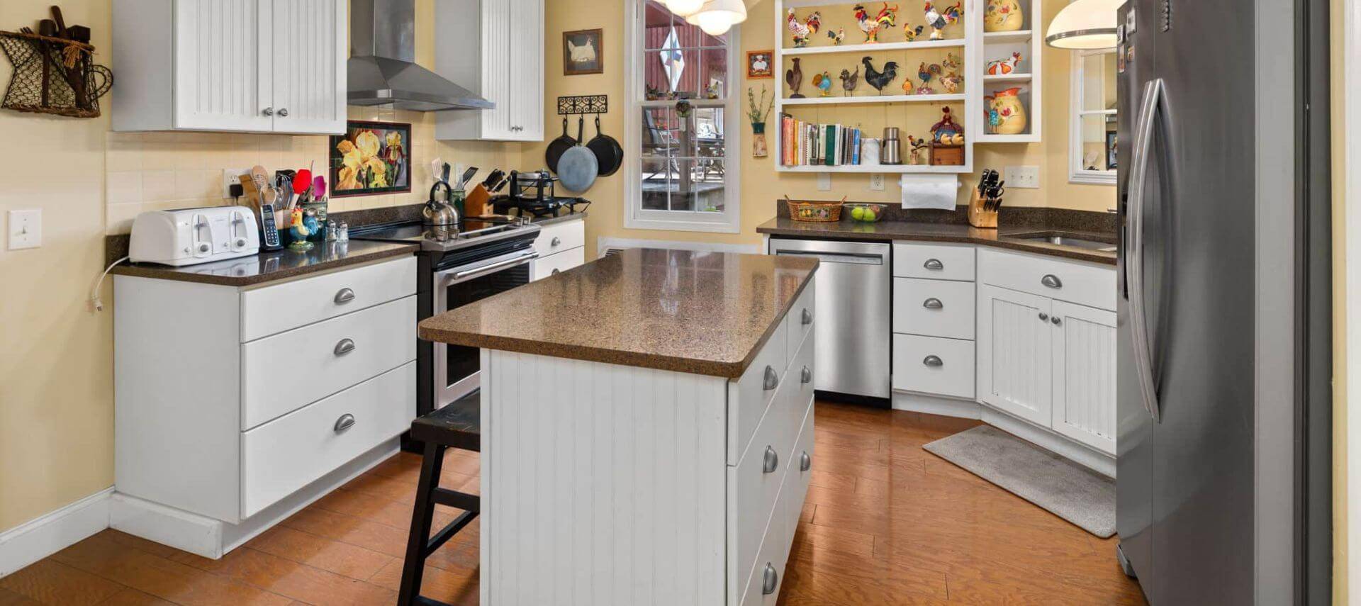 Kitchen with yellow walls, white trim, hardwood flooring, stainless steel appliances, white cabinets, and quartz countertops