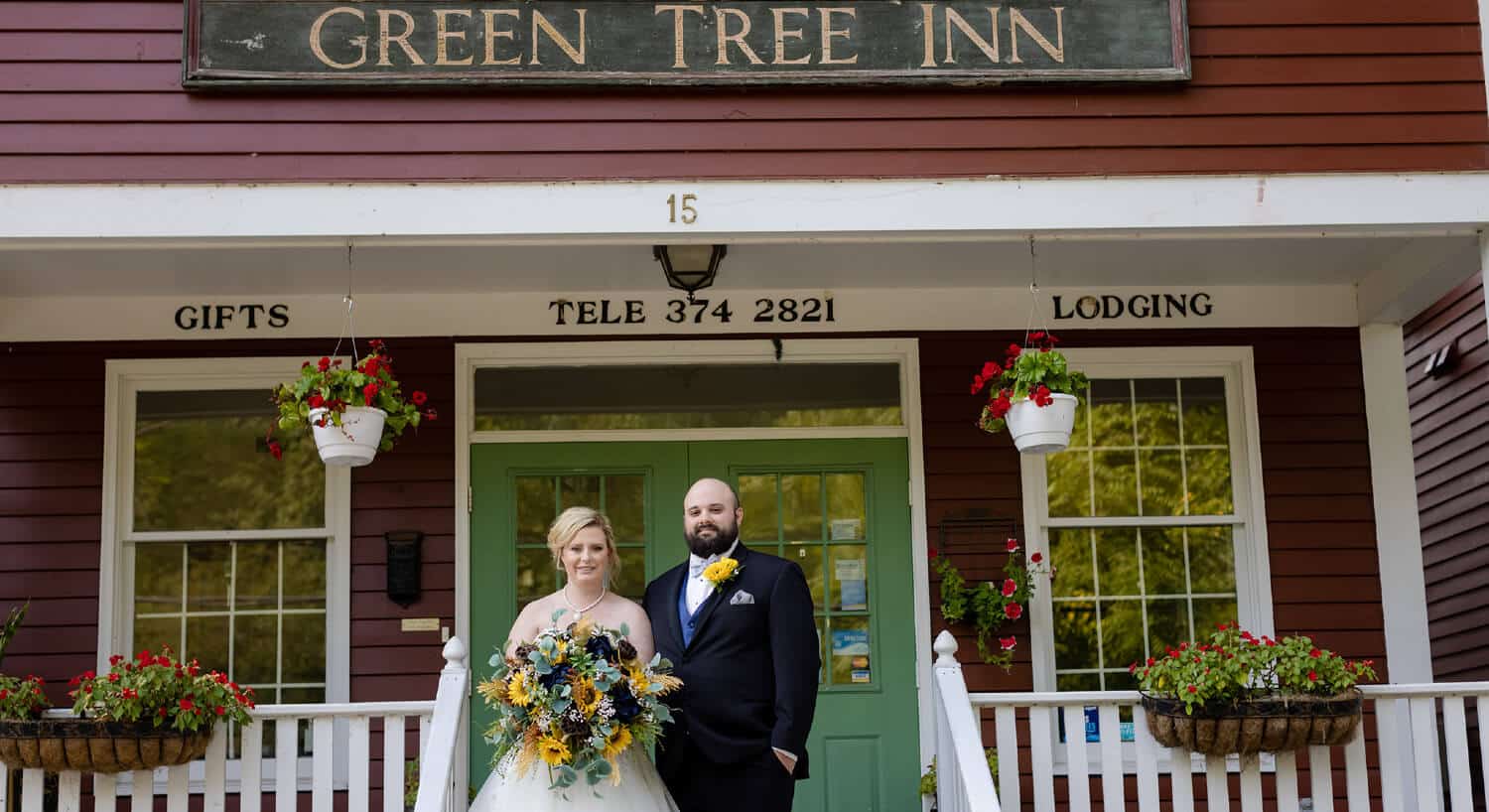 Bride and groom standing on stairs leading onto porch with green sign with text Green Tree Inn hanging on red sided building.